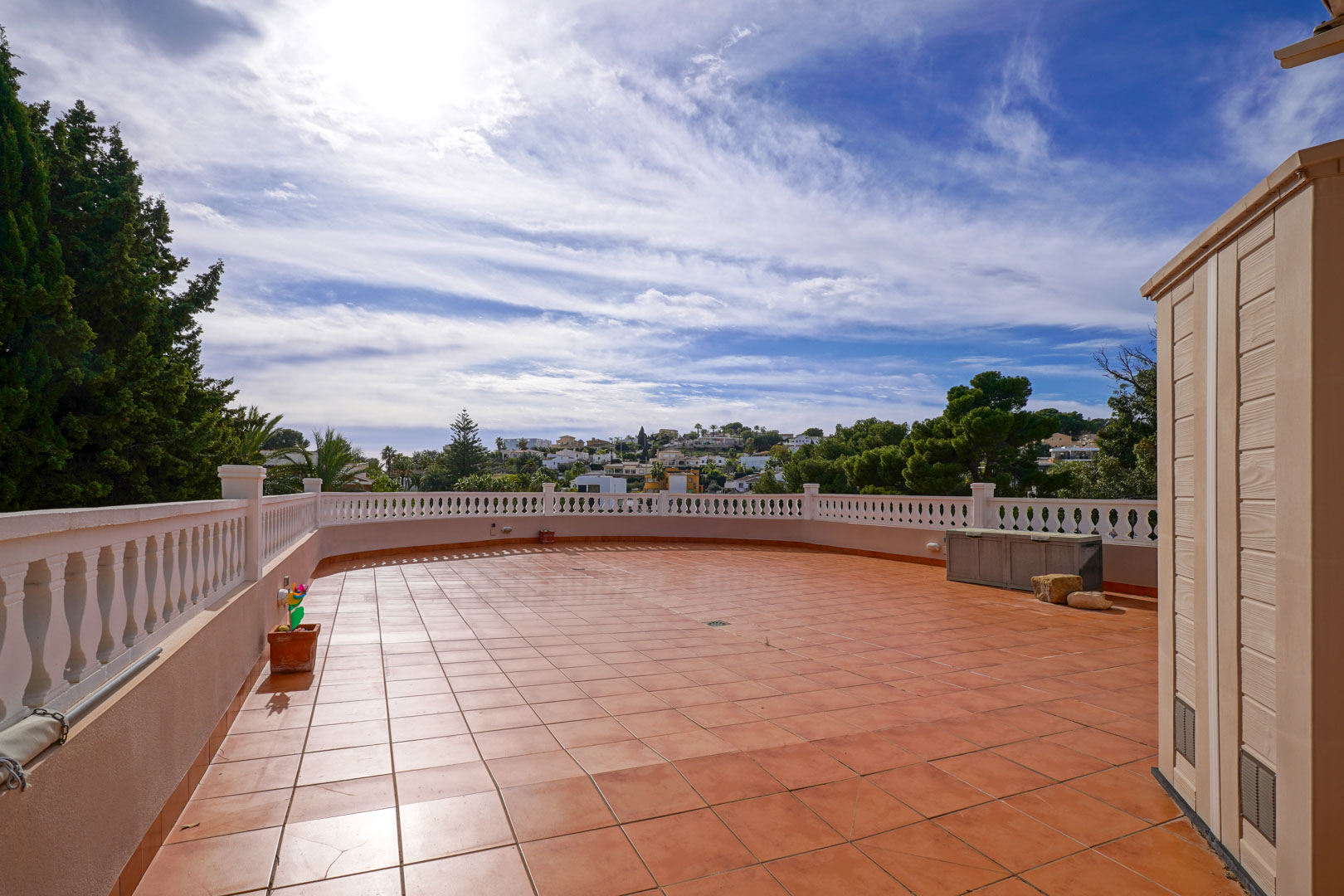 Weitläufige Außenterrasse mit Terrakotta-Fliesen und weißer Balustrade, die einen freien Blick auf die umliegende mediterrane Landschaft bietet.