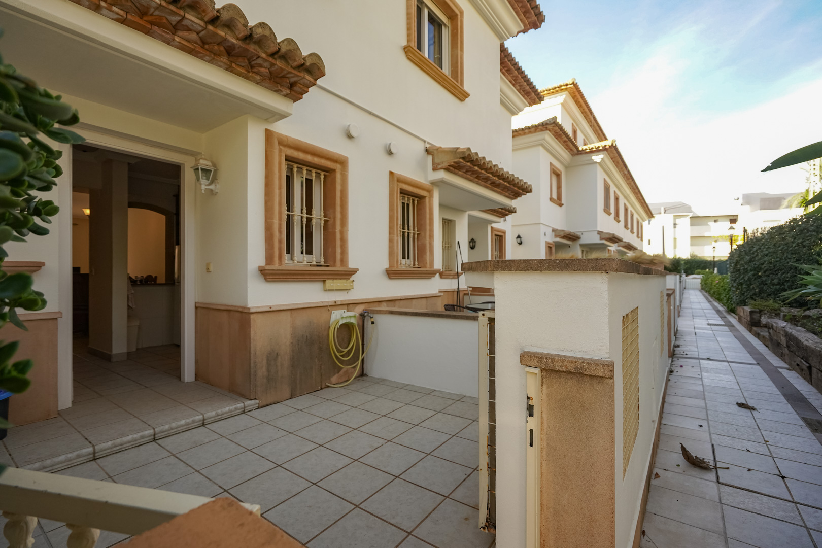 Außenfassade des Triplex-Hauses mit gefliester Vorderterrasse, Fenstereinfassungen aus Tosca-Stein und direktem Zugang vom Fußweg der Wohnanlage.