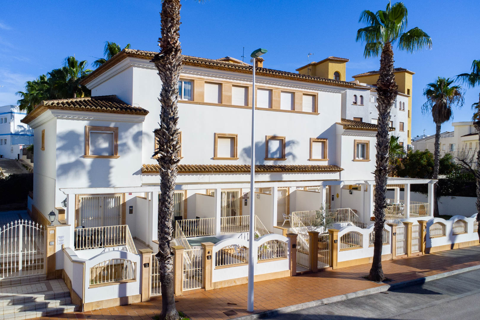 Außenfassade von Triplex-Reihenhäusern im mediterranen Stil mit weißen Wänden, Steinumrandungen und privaten, umzäunten vorderen Terrassen.