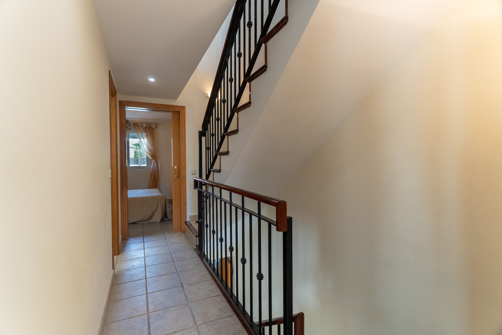 Flur mit Keramikfliesen, der zu den Schlafzimmern führt, mit einer Treppe mit Holzhandlauf und schwarzen Schmiedeeisen-Balustern.