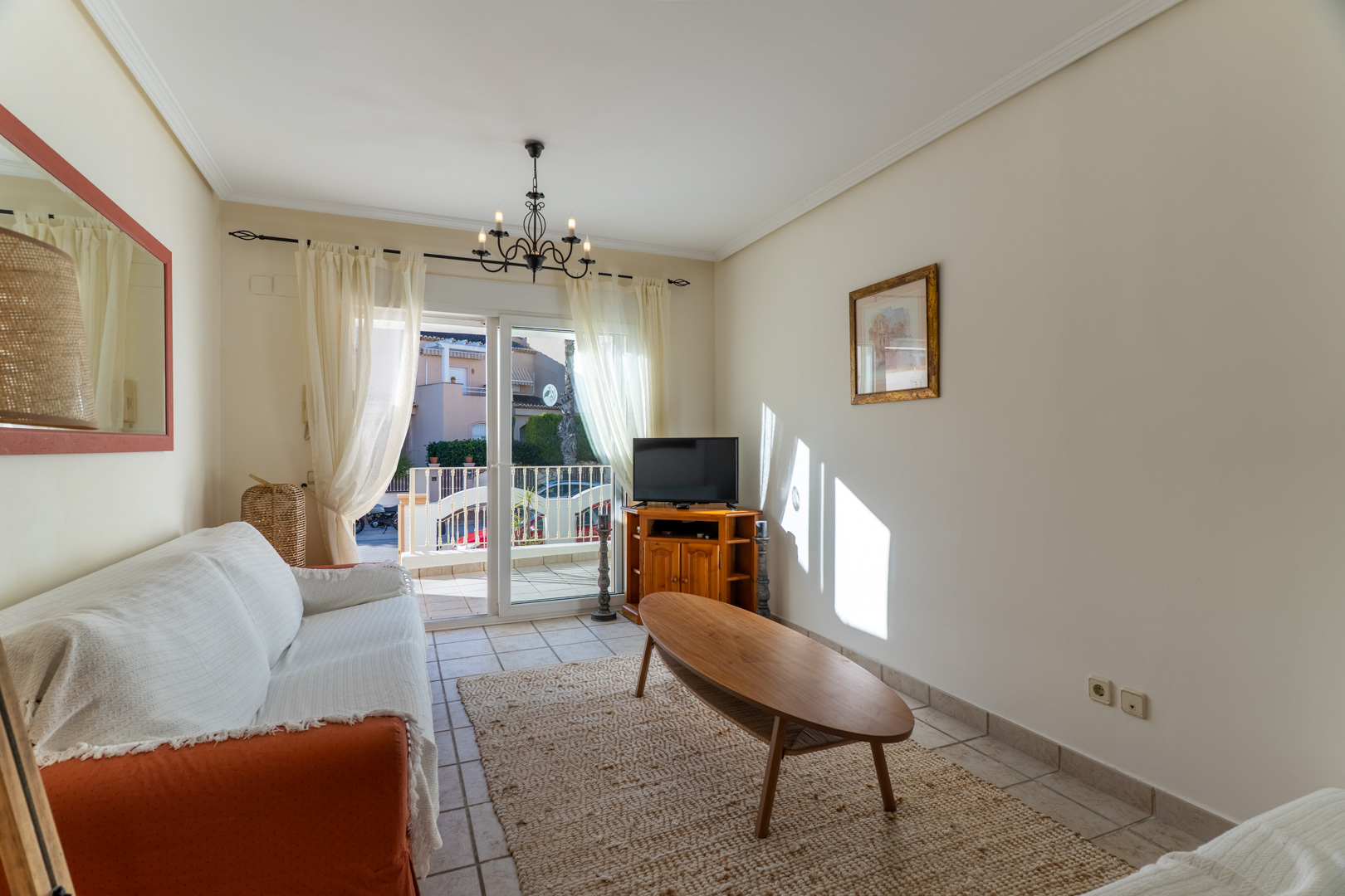 Heller Wohnbereich mit Fliesenboden, ovalem Couchtisch aus Holz und direktem Zugang zur privaten Terrasse durch Glasschiebetüren.