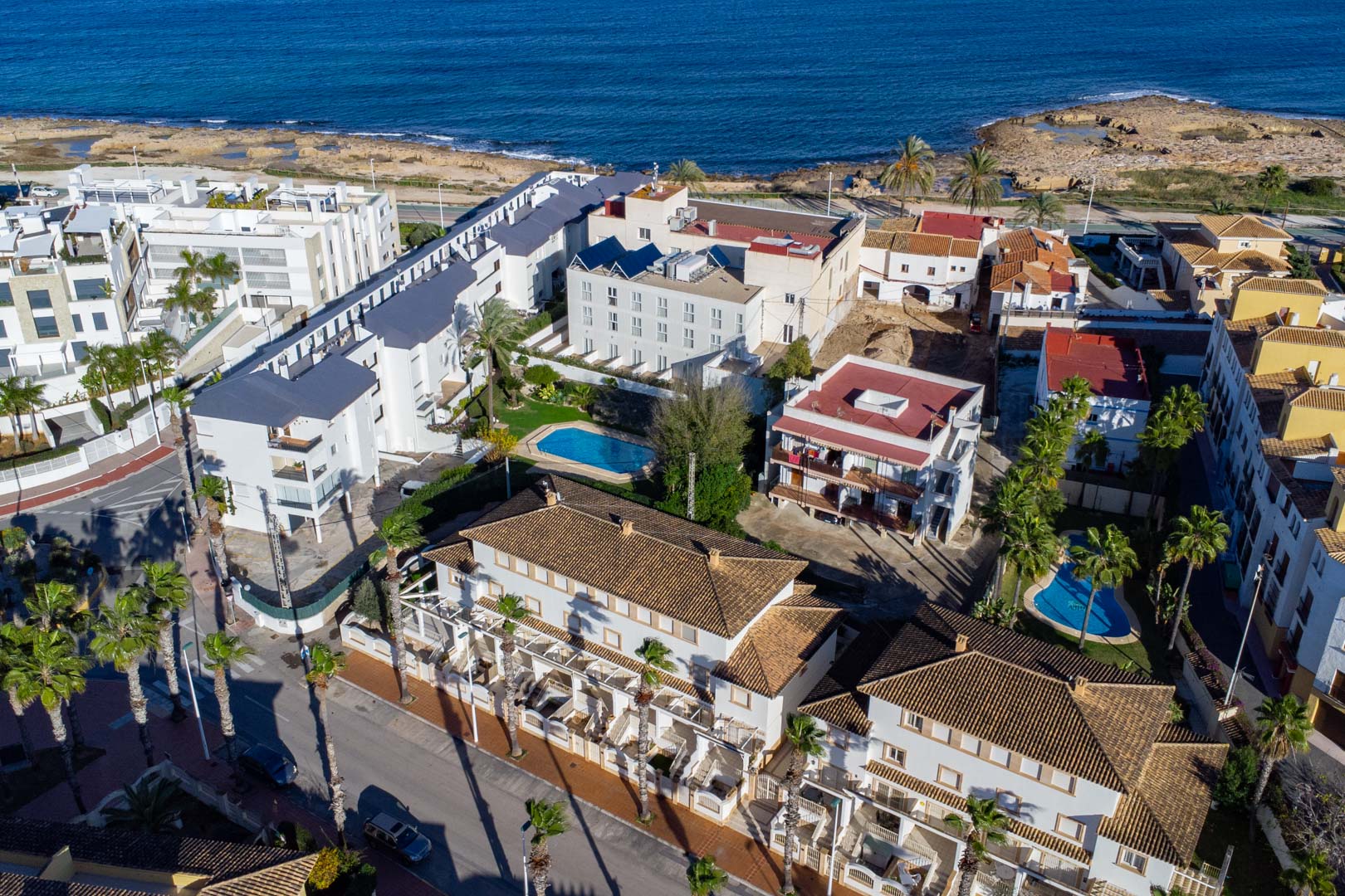 Luftaufnahme der Wohnanlage in der Calle Génova mit Blick auf das Mittelmeer, die Gemeinschaftspools und die traditionellen Ziegeldächer.