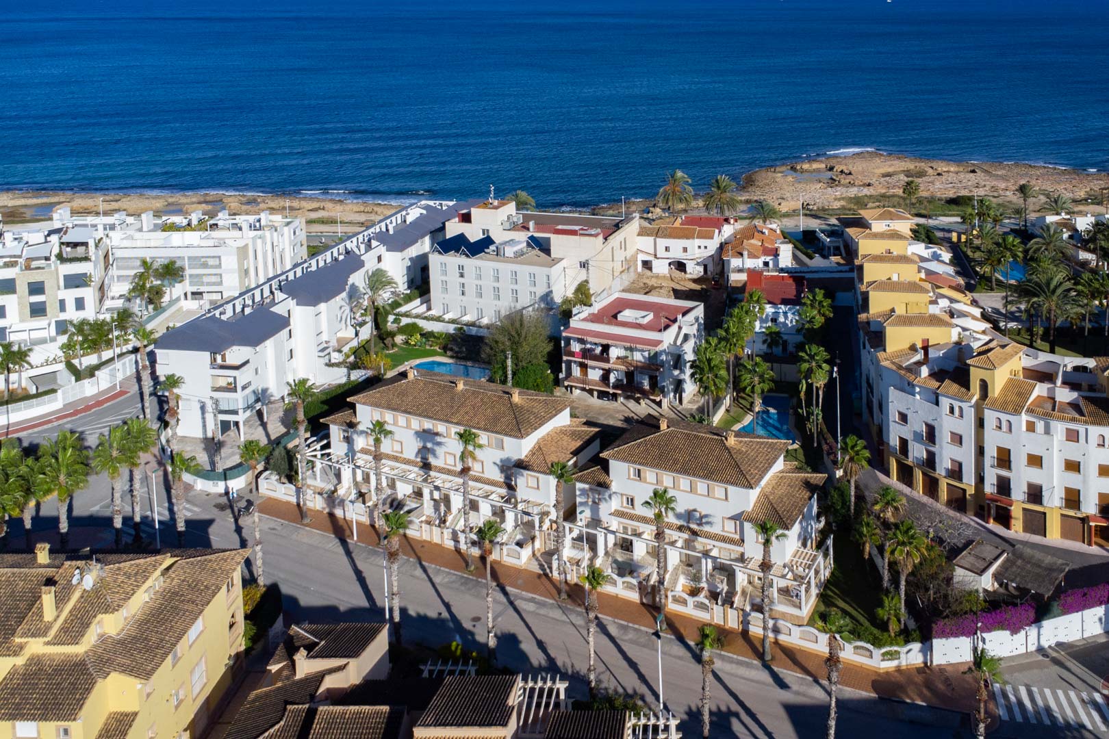 Luftaufnahme des Komplexes in der Calle Génova, die die Nähe zum Mittelmeer und die Architektur mit weißen Fassaden, Ziegeldächern und Palmen verdeutlicht.