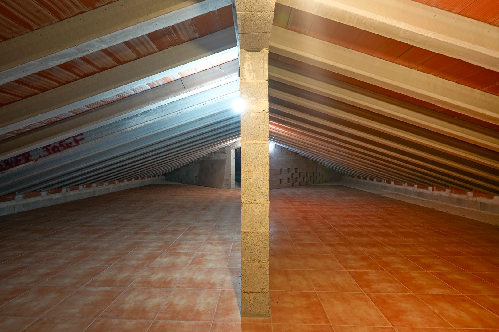 Ausgebauter Dachboden mit Dachschräge, sichtbaren Betonbalken, Terrakotta-Deckenelementen und gefliestem Boden.