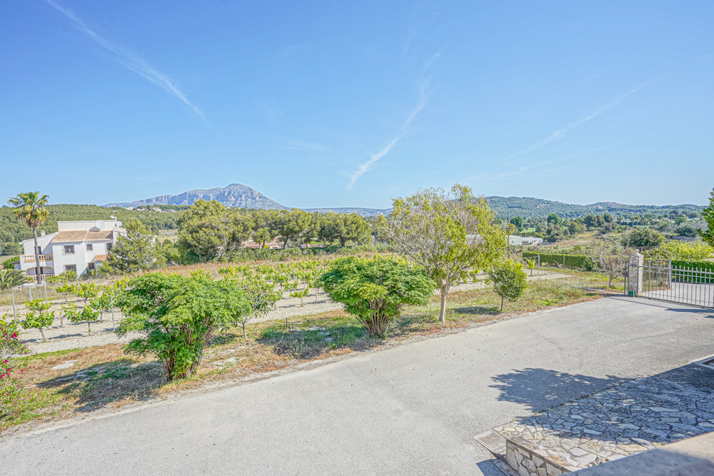 Blick von der gepflasterten Einfahrt auf einen privaten Weinberg und die mediterrane Landschaft mit dem Berg Montgó im Hintergrund.