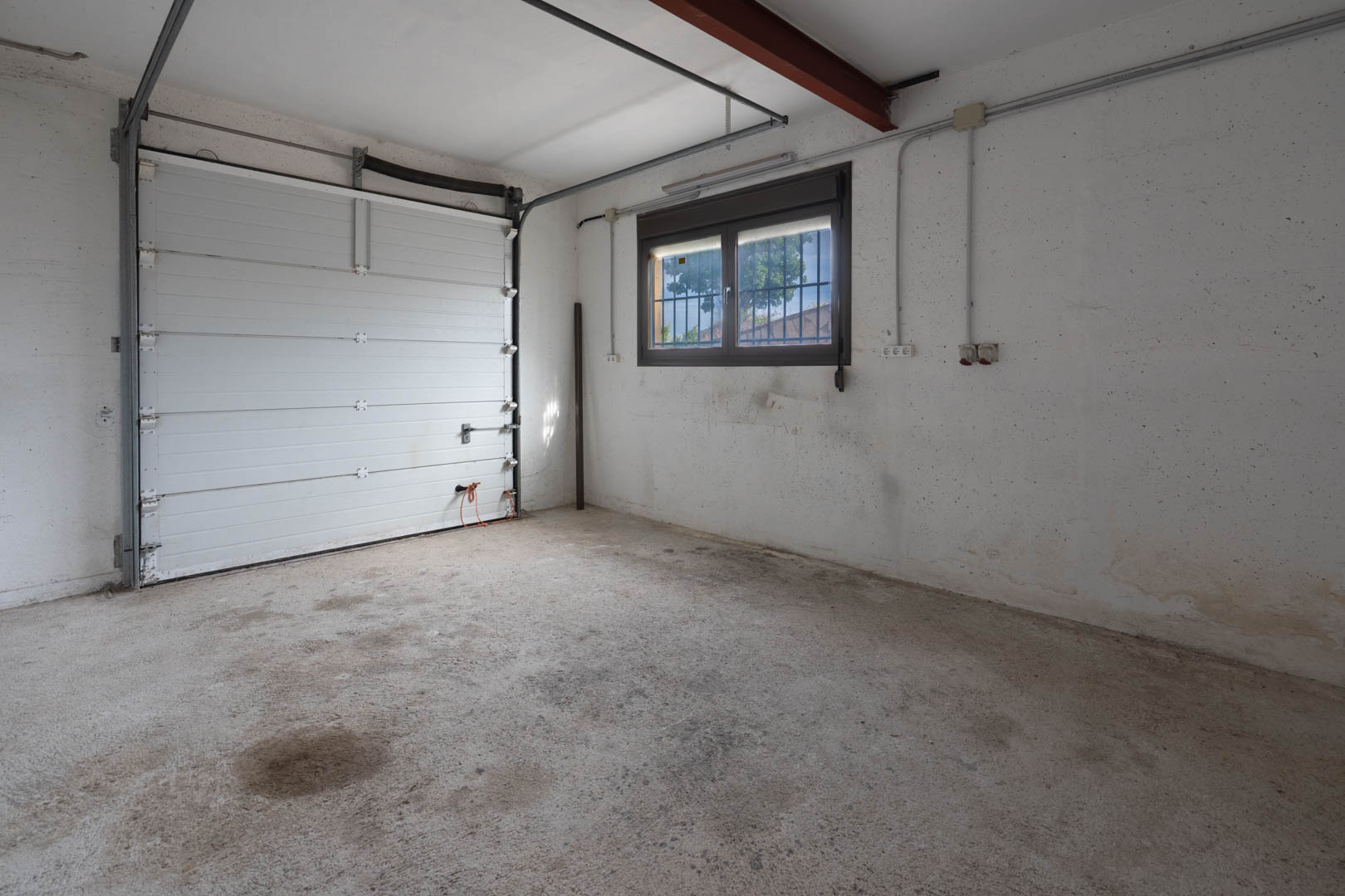 Funktionale Garage mit Betonboden, weißem Sektionaltor und einem vergitterten Fenster für natürlichen Lichteinfall.