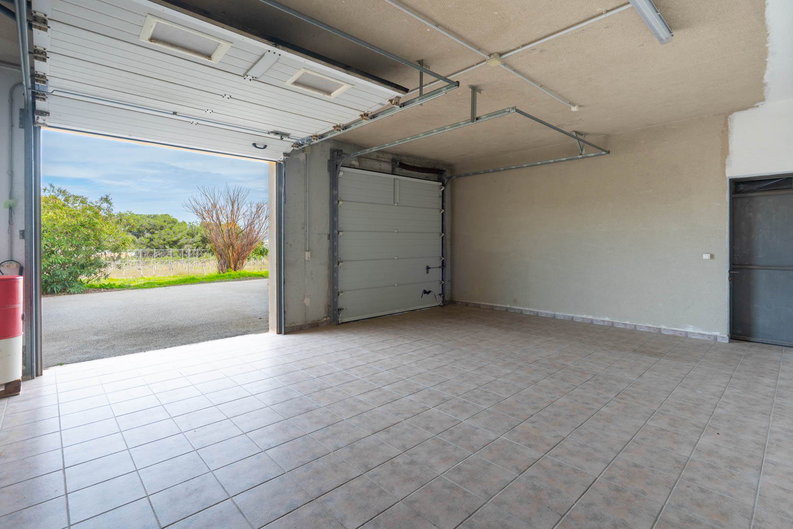 Geräumige Garage mit Fliesenboden, ausgestattet mit zwei Sektionaltoren und Deckenbeleuchtung. Bietet direkten Zugang zur Einfahrt und zum Garten.