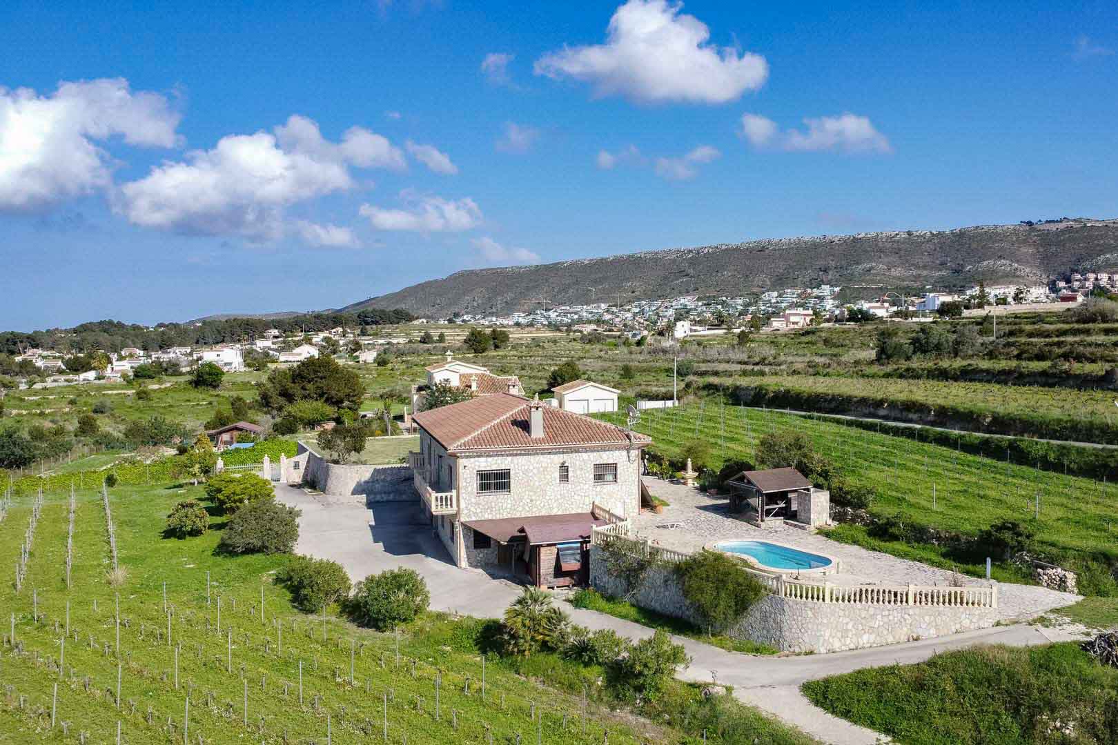 Luftaufnahme einer Natursteinvilla mit Außenpool, Sonnenterrasse mit Balustraden und weitläufigen Weinbergen in hügeliger, ländlicher Umgebung.
