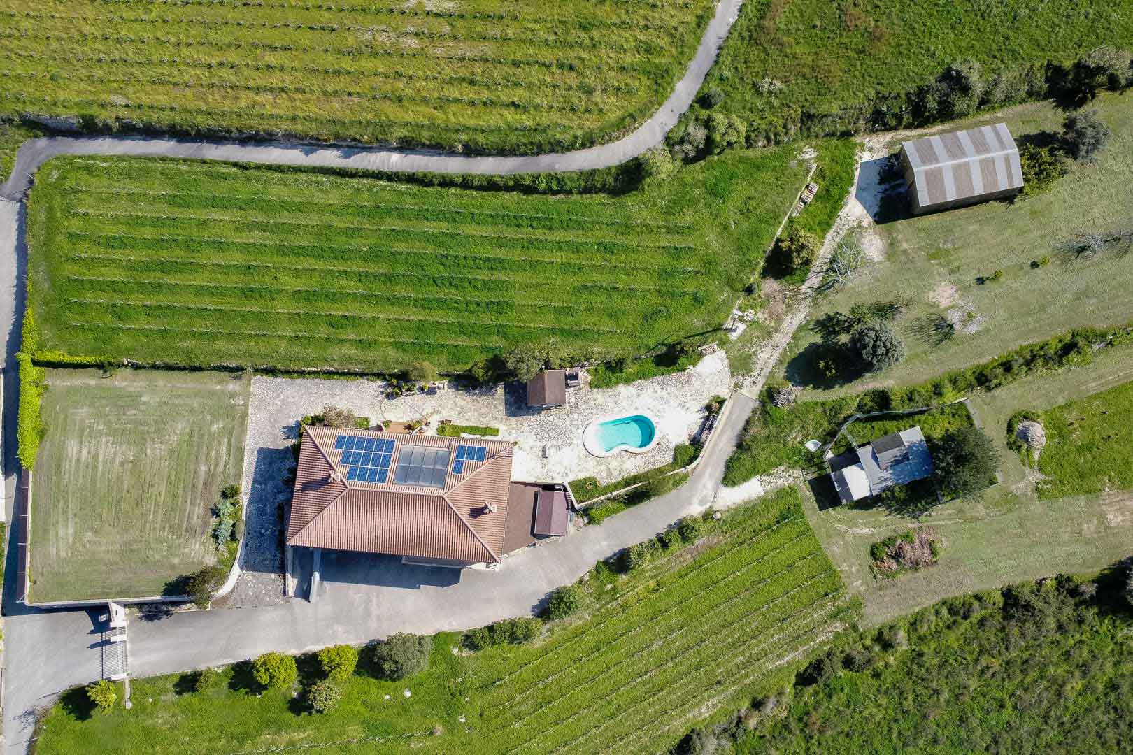 Luftaufnahme eines Anwesens mit Solaranlage, nierenförmigem Außenpool und großflächigen landwirtschaftlichen Nutzflächen in grüner Umgebung.