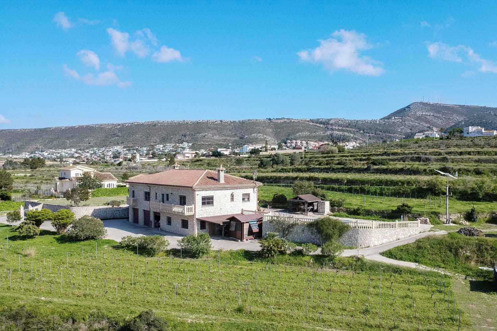 Luftaufnahme eines zweistöckigen Steinlandhauses mit Terrakottadach, umgeben von Weinbergen und terrassierten Feldern vor einer markanten Bergkulisse.