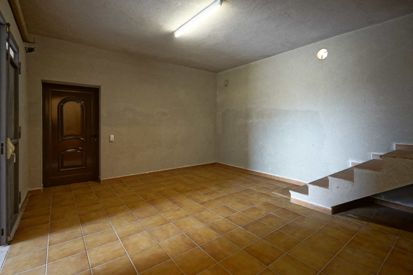Mehrzweckraum mit rustikalen Terrakottafliesen, verputzten Wänden und einer gefliesten Treppe zum Obergeschoss.