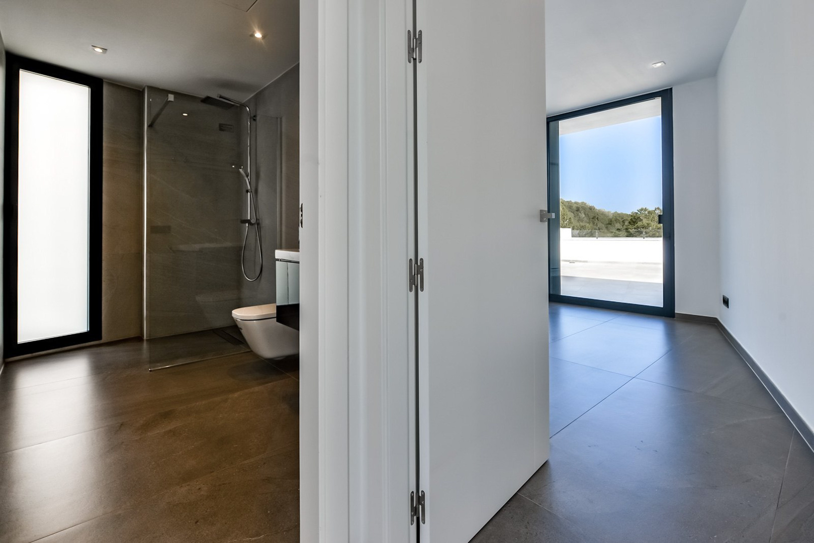 Hauptschlafzimmer mit En-Suite-Bad, begehbarer Dusche, großformatigen Fliesen und direktem Zugang zur Terrasse durch bodentiefe Schiebefenster.