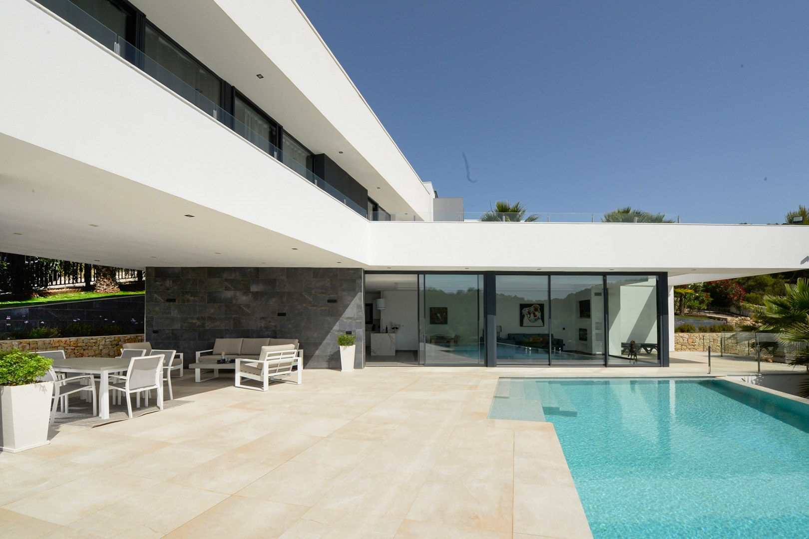 Hauptterrasse mit Infinity-Pool, überdachtem Essbereich im Freien und minimalistischer Architektur mit bodentiefen Glasfronten und Natursteinakzenten.