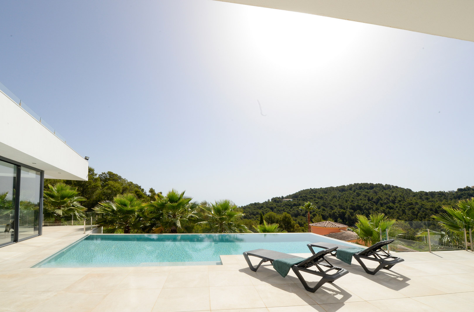 Infinity-Pool und Sonnenterrasse mit Liegestühlen, die einen weiten Blick über die grünen Hügel und die mediterrane Landschaft bieten.