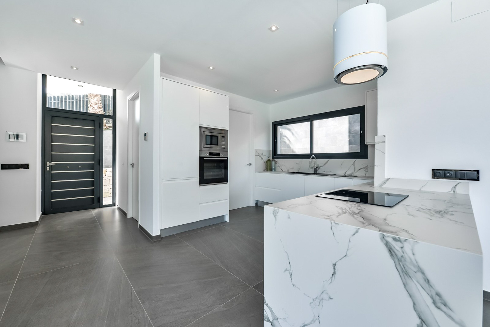 Moderne Designerküche mit Kochinsel in Marmoroptik, integrierten Geräten und zylindrischer Dunstabzugshaube neben der schwarzen Eingangstür.