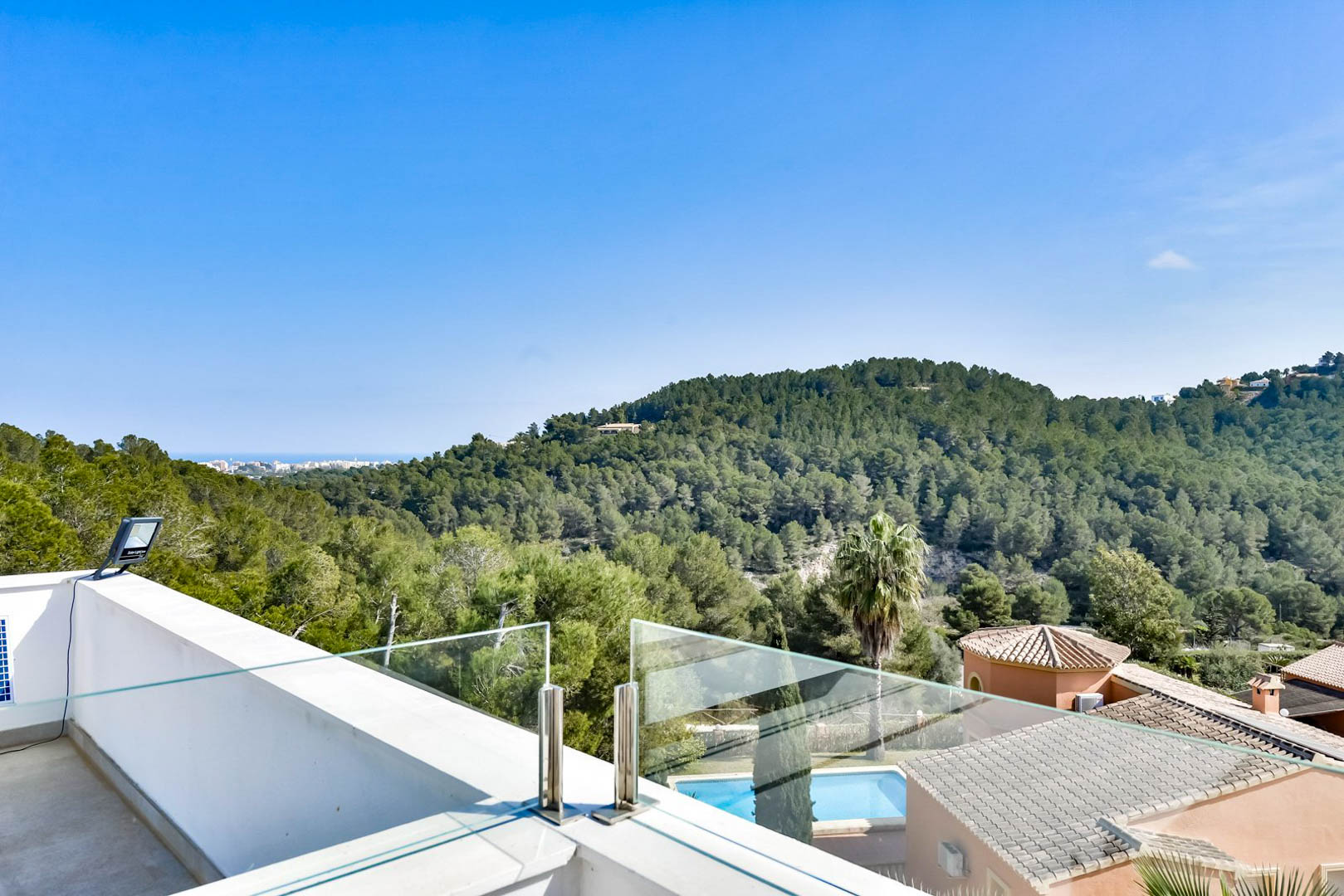 Obere Terrasse mit Glasbalustrade und Edelstahlbeschlägen, die einen weiten Blick über pinienbewachsene Hügel bis hin zum Mittelmeer bietet.