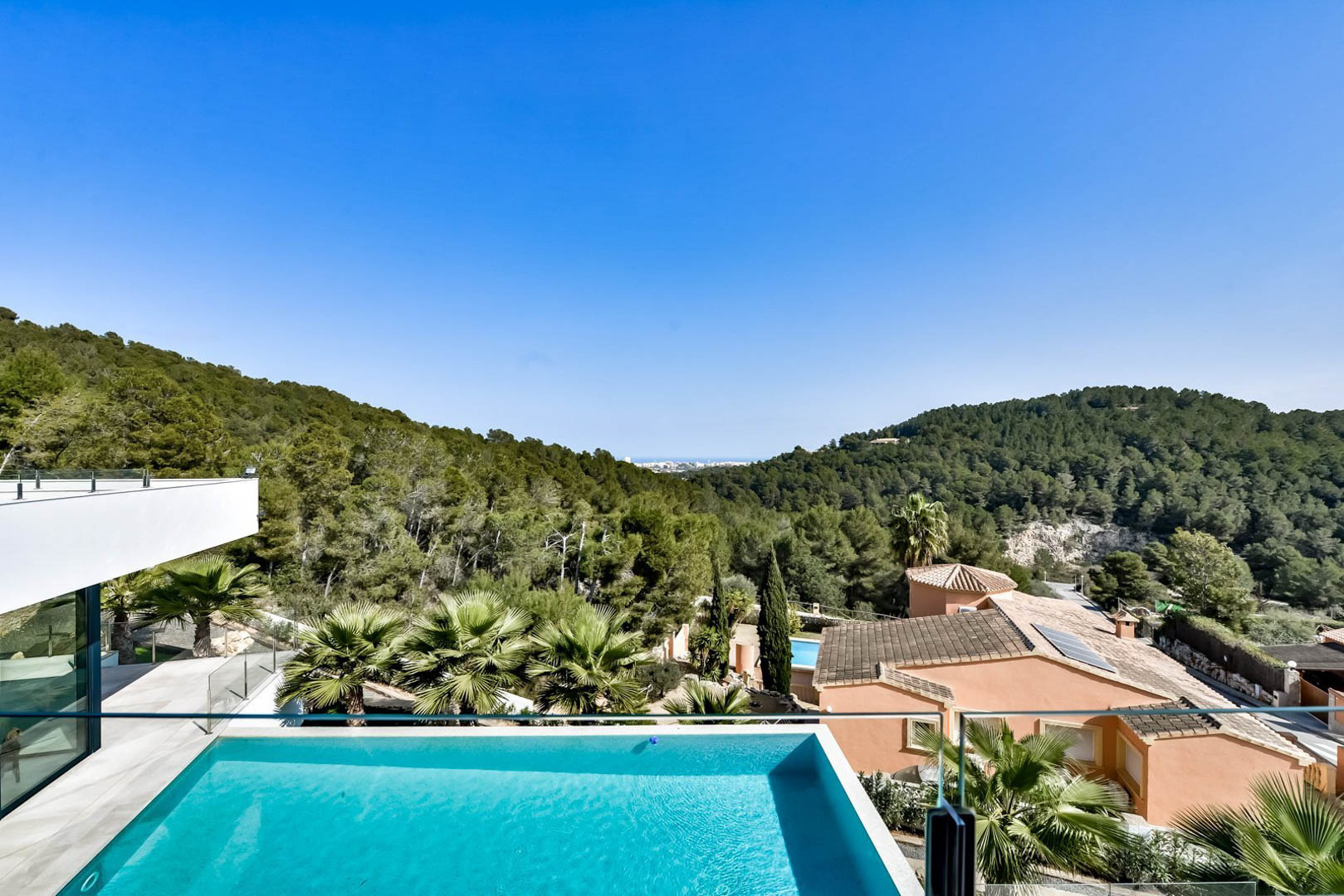 Panoramablick von der oberen Terrasse mit Infinity-Pool, Glasgeländer und weitem Ausblick über die bewaldeten Hügel von Jávea bis hin zum Meer.