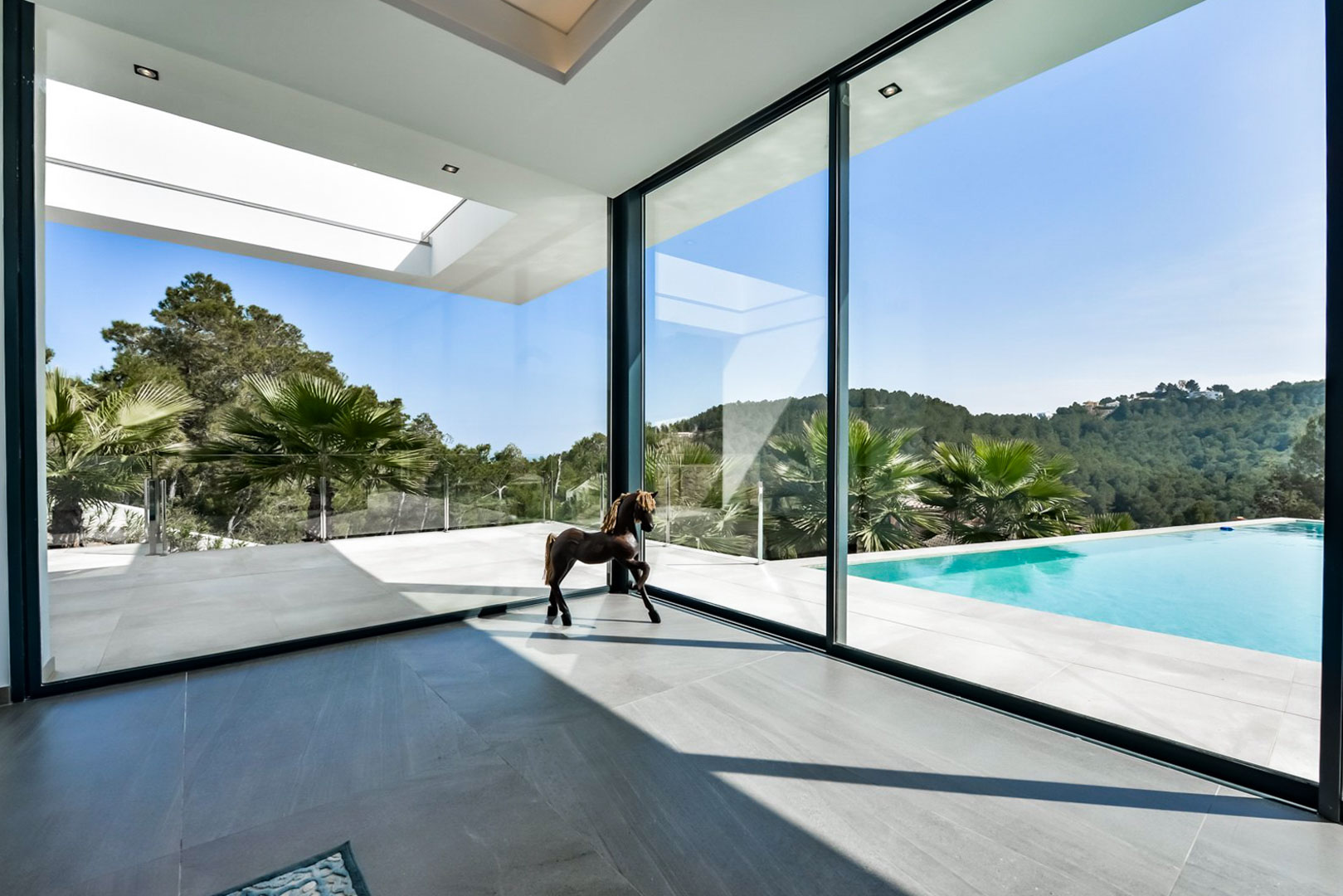 Wohnbereich mit bodentiefen Glasfronten, die den Blick auf die Terrasse mit Infinity-Pool und die umliegende Hügellandschaft von Jávea freigeben.