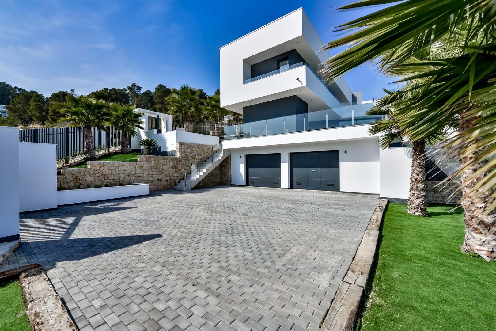 Zeitgenössische Fassade mit Doppelgarage, Natursteinmauern und gepflasterter Einfahrt, umgeben von mediterraner Bepflanzung.