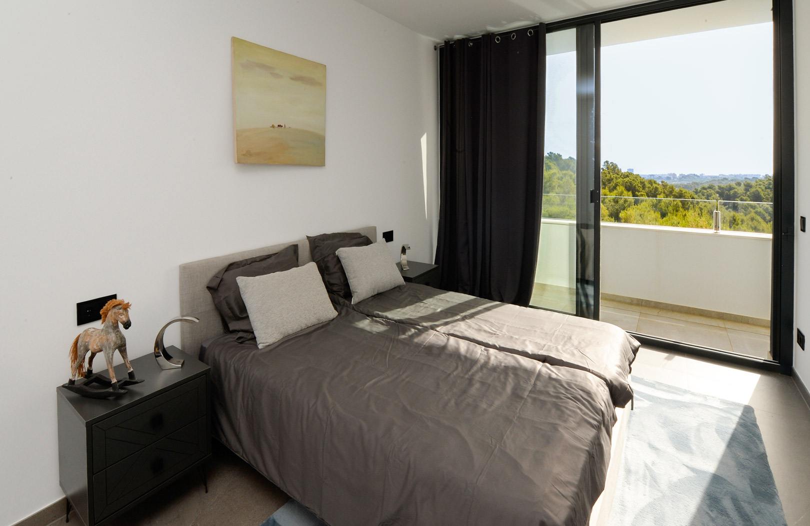 Zeitgenössisches Schlafzimmer mit direktem Terrassenzugang, bodentiefen Glasfronten mit Blick ins Grüne und minimalistischer Einrichtung in Grautönen.