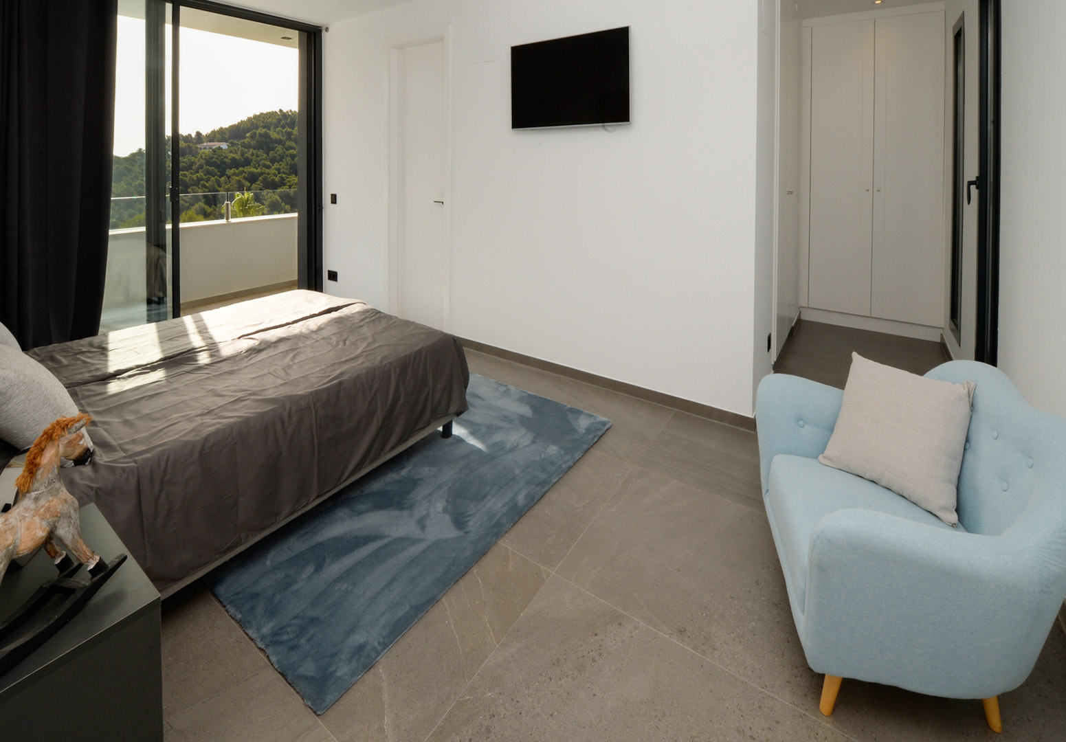 Zeitgenössisches Schlafzimmer mit Terrassenzugang, grauen Fliesen, weißen Einbauschränken und Panoramablick auf die umliegende Natur.