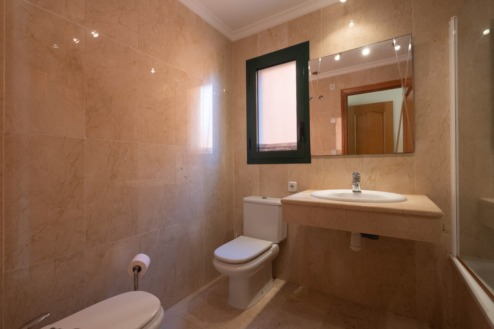 Badezimmer mit cremefarbenem Marmor an Wänden und Boden, integriertem Waschtisch aus Naturstein und einem Fenster für natürliches Licht und Belüftung.