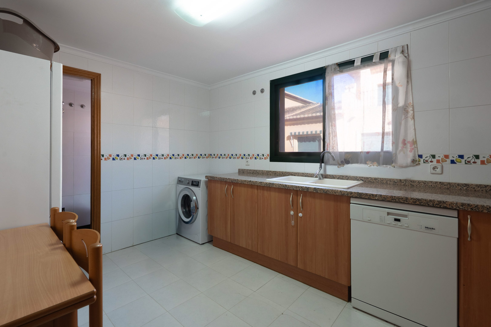 Funktionale Küche mit Granitarbeitsplatte, Holzschränken, integriertem Waschbereich und einem Fenster für natürliches Licht.