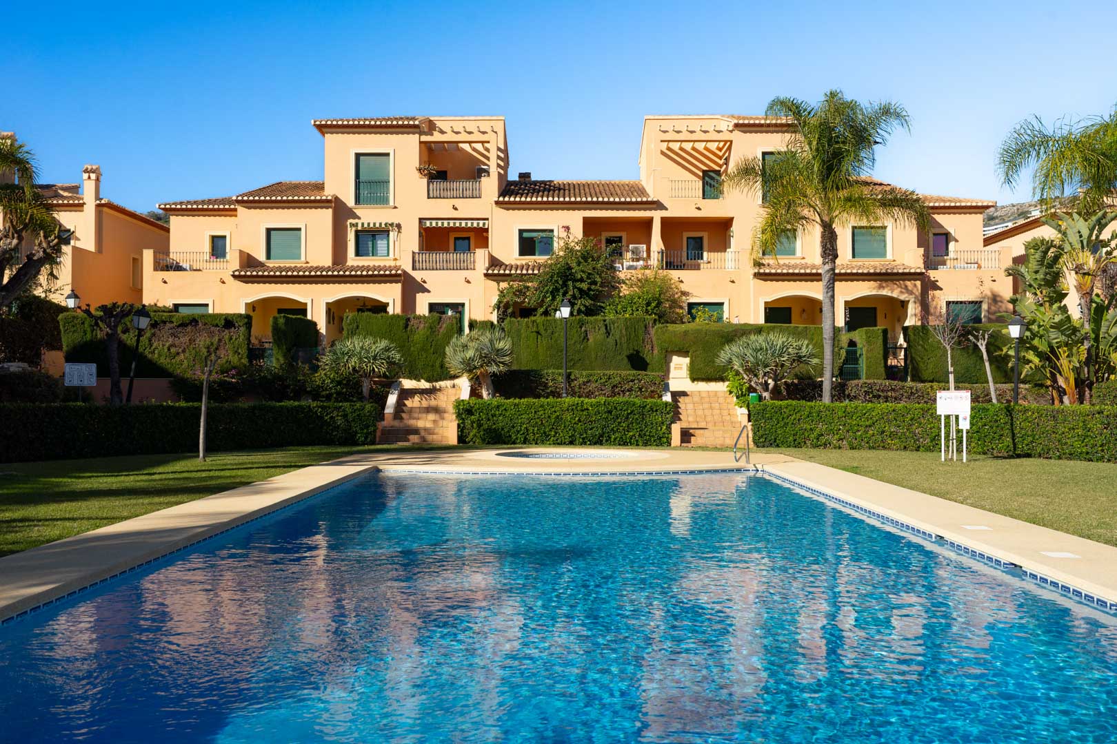 Gemeinschaftspool umgeben von gepflegten mediterranen Gärten und Rasenflächen, mit der traditionellen Architektur der Floridamar-Anlage im Hintergrund.