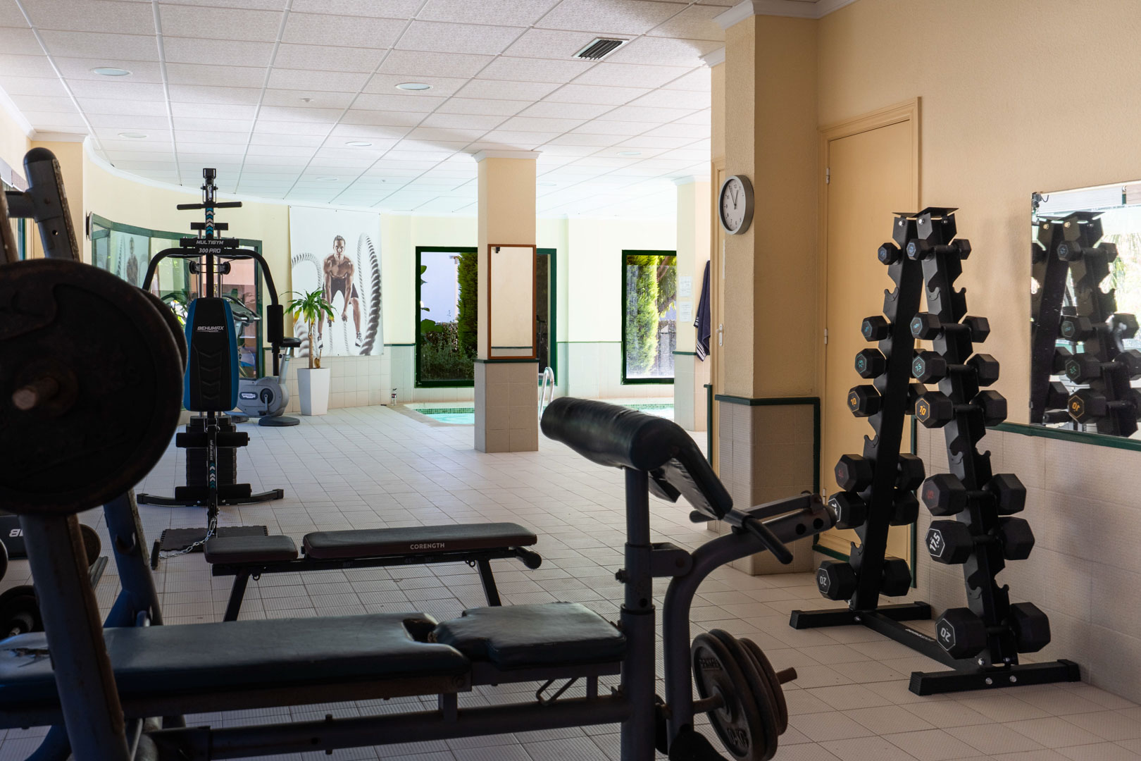 Hauseigenes Fitnessstudio mit Kraftgeräten und Hantelstation, direkt neben dem Hallenbad mit Blick auf die gepflegte Gartenanlage gelegen.