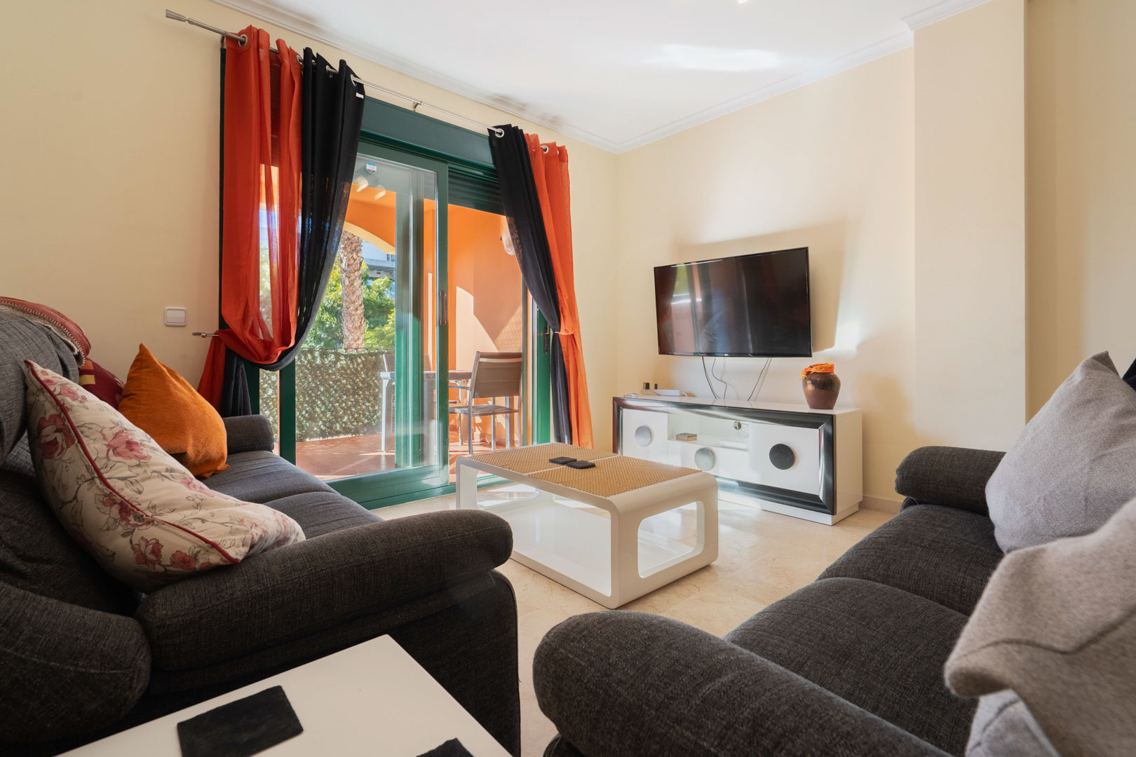 Heller Wohnbereich mit dunkelgrauen Sofas, Marmorböden und direktem Zugang zur privaten Terrasse durch große Glasschiebetüren.