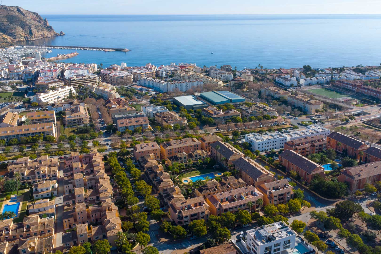 Luftaufnahme der Anlage Floridamar in Jávea, die den zentralen Poolbereich und die Nähe zum Hafen sowie zur Mittelmeerküste verdeutlicht.