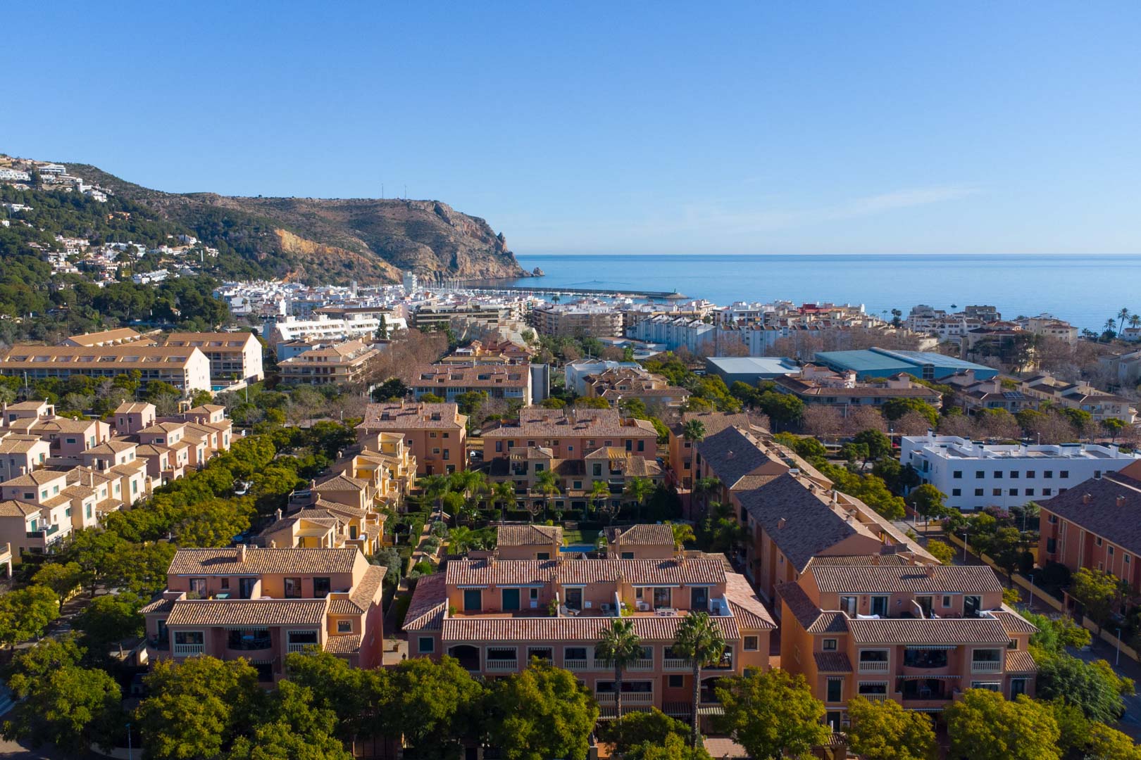 Luftaufnahme der Anlage Floridamar in Jávea mit ihrer mediterranen Architektur, üppigen Grünflächen und Blick auf den Hafen sowie das Cabo de San Antonio.