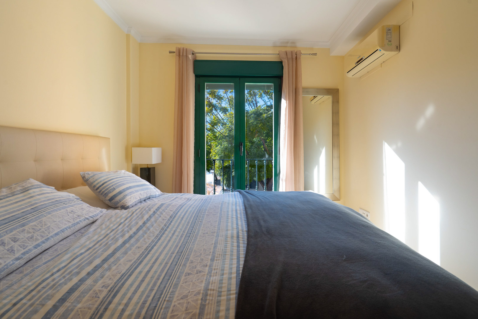 Schlafzimmer mit Doppelbett, Klimaanlage und grünen Balkontüren. Der Raum bietet viel natürliches Licht und einen Blick auf die Vegetation.