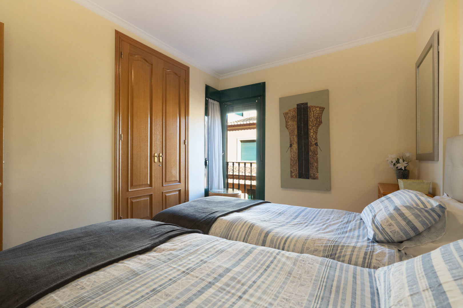 Schlafzimmer mit zwei Einzelbetten, Einbauschrank aus Holz und Zugang zu einem Balkon mit traditionellen grünen Fensterläden.