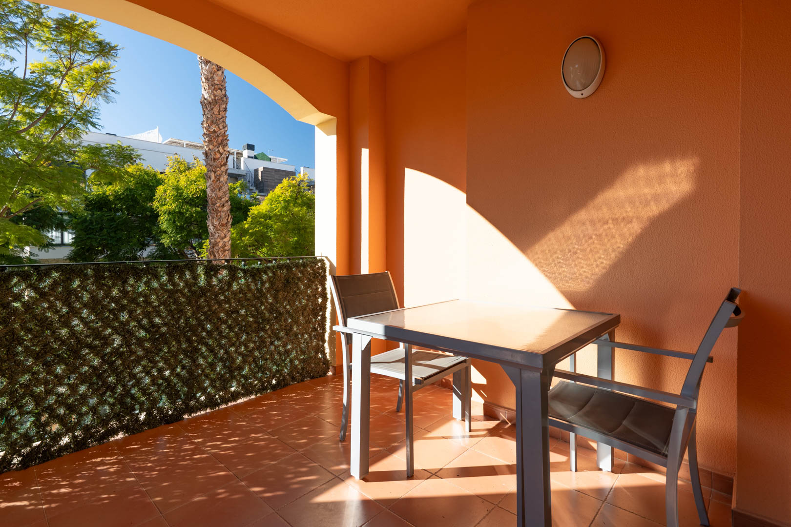 Überdachte Terrasse mit Terrakottaboden, moderner Sitzgruppe und Blick auf die gepflegten mediterranen Gärten der Anlage.