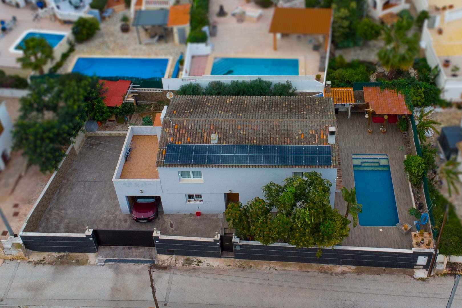 Luftaufnahme der Villa mit Photovoltaikanlage auf dem Ziegeldach, privatem Pool mit Sonnenterrasse und integrierter Garage auf einem umzäunten Areal.
