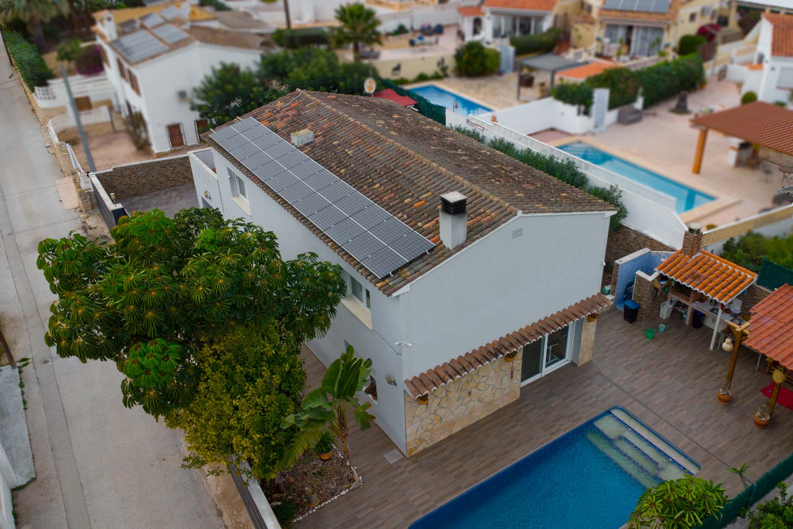 Luftaufnahme der Villa mit Photovoltaikanlagen auf dem Dach, einem privaten Pool und einem Außen-Grillbereich auf der gefliesten Terrasse.