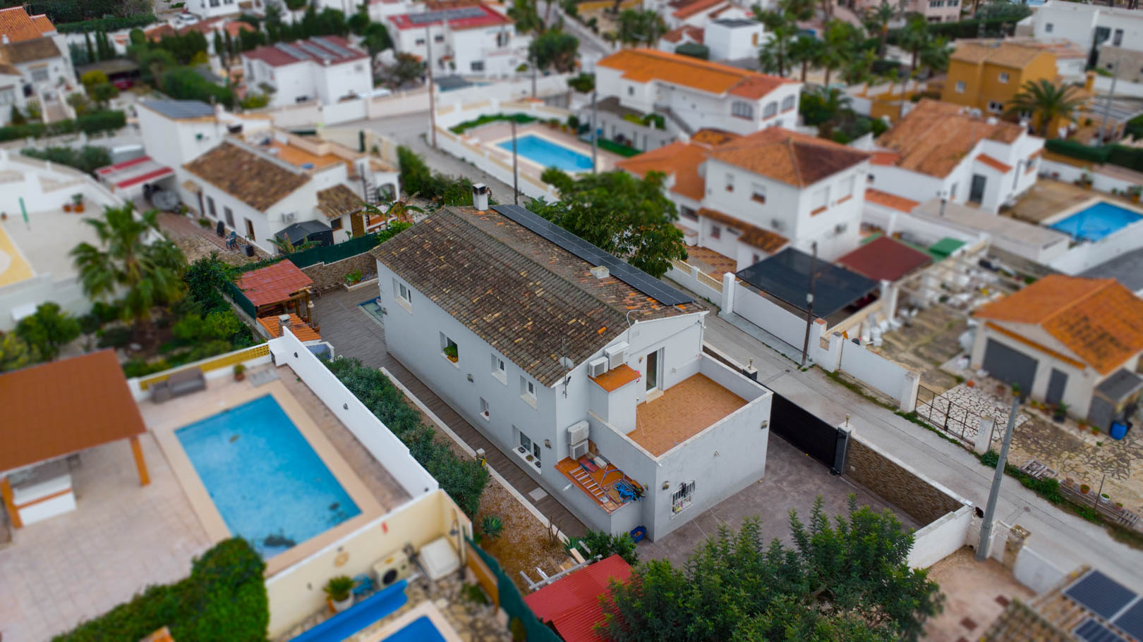 Luftaufnahme der Villa mit Photovoltaikanlagen auf dem Ziegeldach, einer Terrasse im Obergeschoss und der Einbettung in die gepflegte Wohngegend.