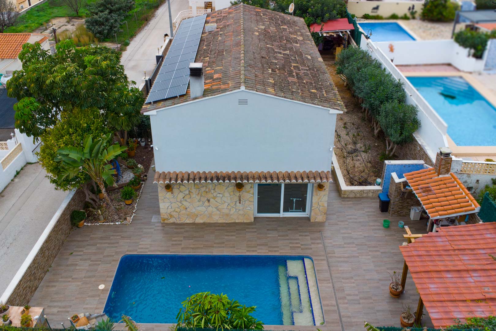 Luftaufnahme der Villa mit Solarmodulen auf dem Dach, privatem Pool und gepflasterter Terrasse mit überdachtem Grillbereich.