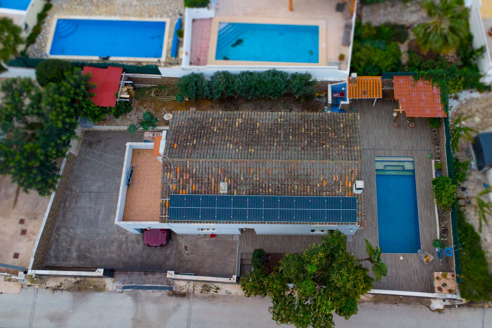 Luftbild der Villa mit Photovoltaik-Modulen auf dem Dach, einem rechteckigen Pool und dem befestigten privaten Parkplatzbereich.