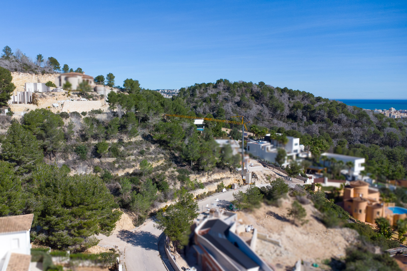 Erhöhte Ansicht der Urbanisation Tosalet 5 in Jávea mit Baugrundstücken in Hanglage, umgeben von Pinien und mit Blick auf das Mittelmeer am Horizont.