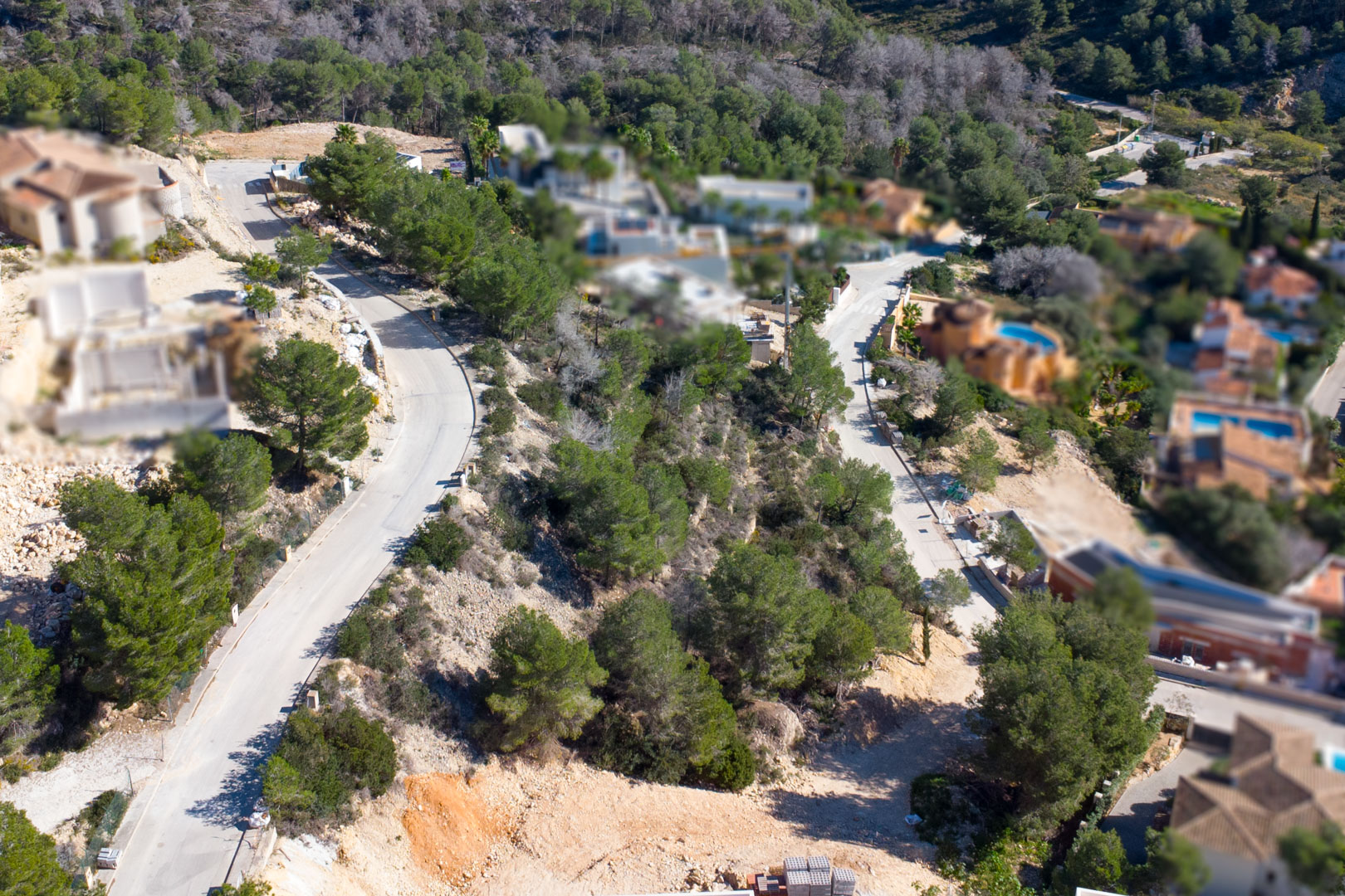 Luftaufnahme der Urbanisation Tosalet 5 in Jávea mit asphaltierten Zufahrtswegen, bewaldeten Baugrundstücken in Hanglage und angrenzenden Villen mit Pool.