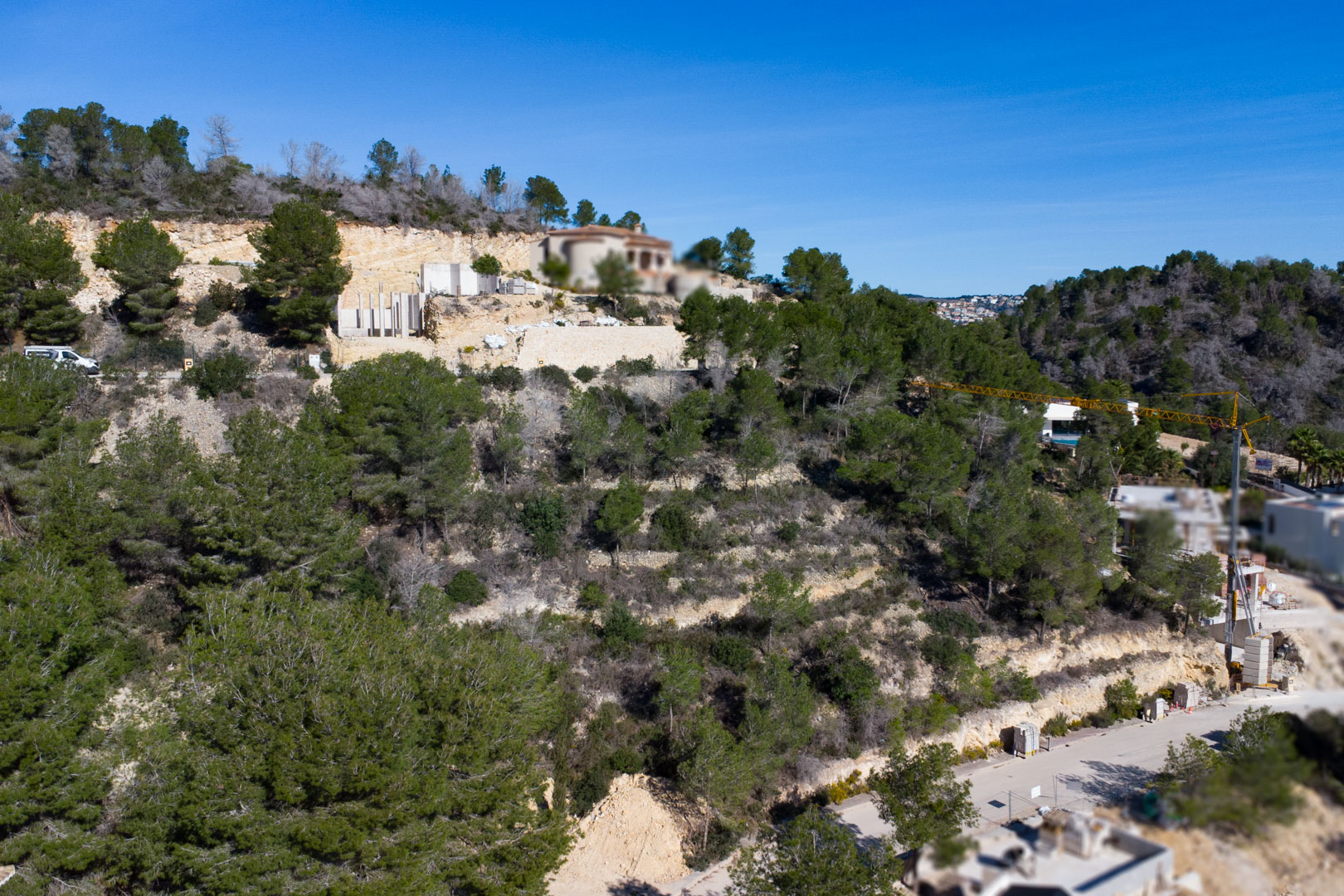 Luftaufnahme eines terrassierten Hanggrundstücks mit mediterranen Pinien, Steinstützmauern und laufenden Bauarbeiten in der Urbanisation Tosalet 5.