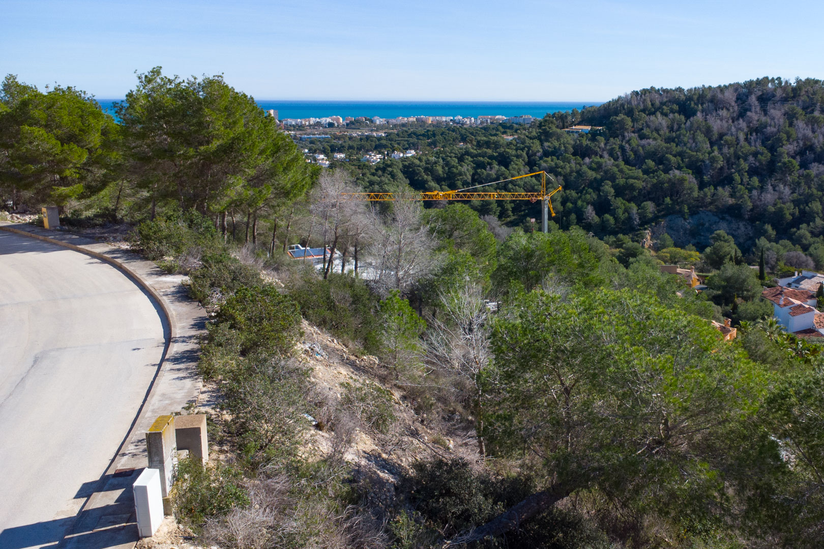 Panoramablick vom erhöhten Grundstück auf das Mittelmeer, mit einheimischen Pinien und der asphaltierten Zufahrtsstraße in der Erschließung Tosalet 5.