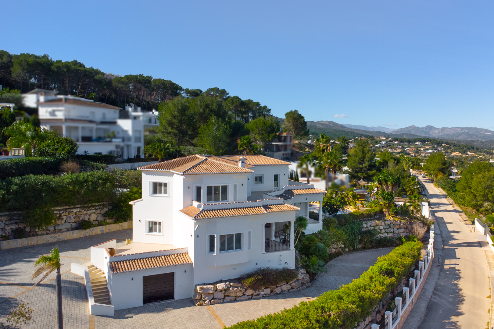 Außenansicht der mehrstöckigen Villa mit weißer Fassade, Terrakottadächern und Natursteinmauern, eingebettet in eine mediterrane Hügellandschaft.