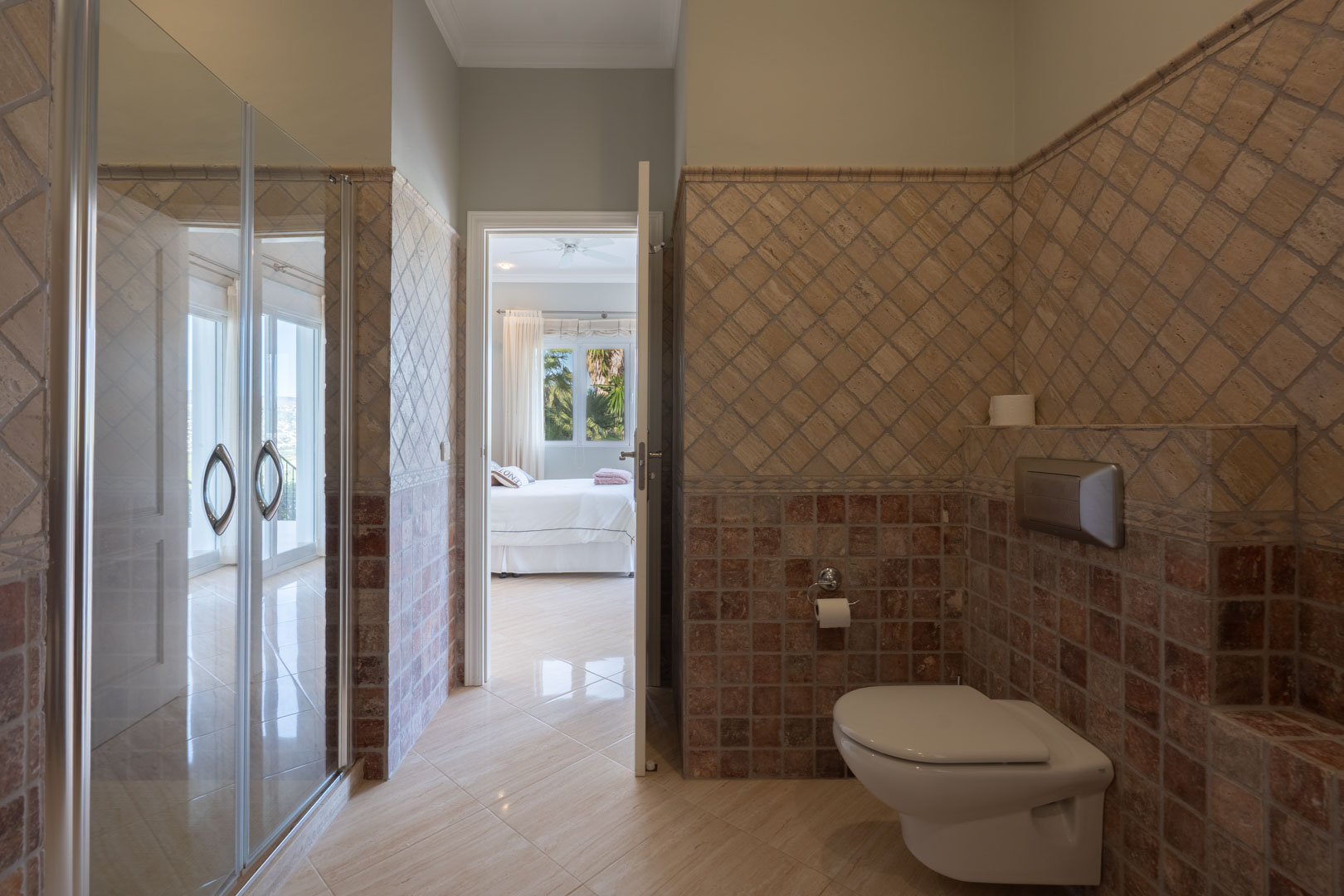 En-Suite-Badezimmer mit rustikalen Natursteinfliesen, Wand-WC und direktem Übergang in das lichtdurchflutete Schlafzimmer.