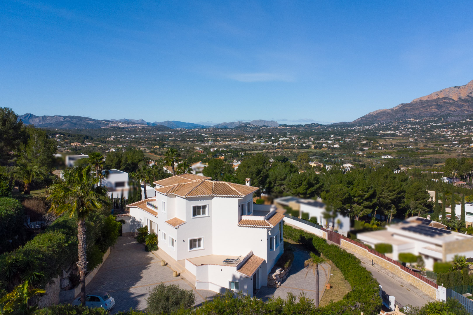 Erhöhte Außenansicht der weißen Villa mit Terrakottadächern, großzügiger gepflasterter Einfahrt und Panoramablick auf das Tal und den Berg Montgó.
