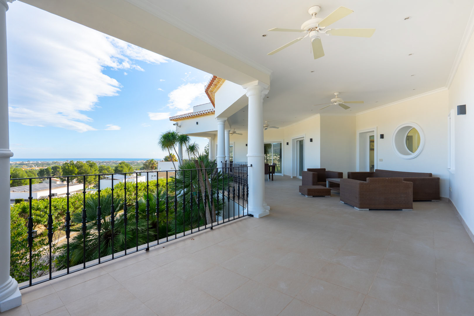 Großzügige überdachte Terrasse mit weißen Säulen, Rattan-Loungemöbeln und Panoramablick auf das Mittelmeer und die Küstenlandschaft.