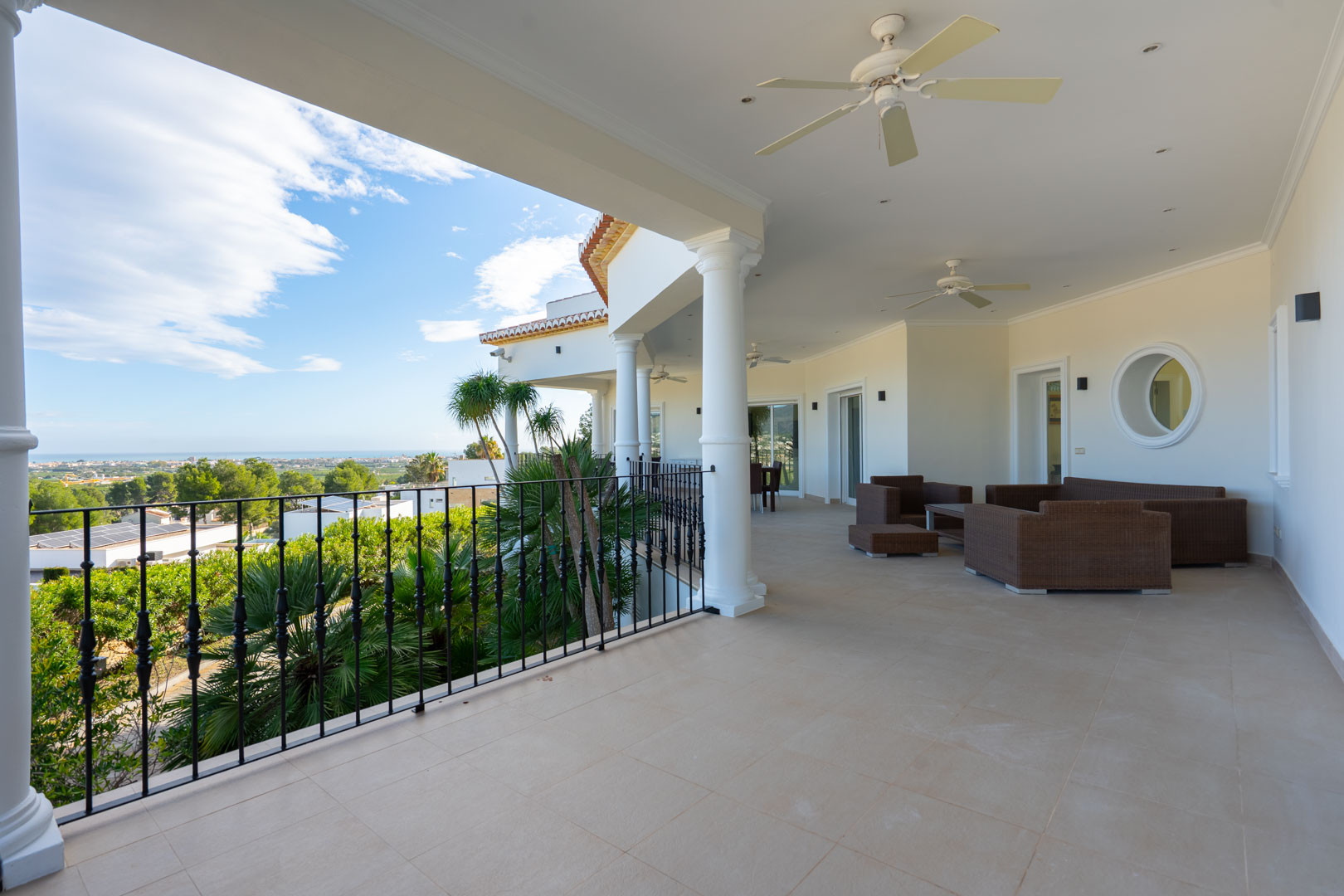 Großzügige überdachte Terrasse mit weißen Säulen, Schmiedeeisengeländer und Fliesenboden. Sie bietet einen Loungebereich mit Panoramablick auf das Meer.