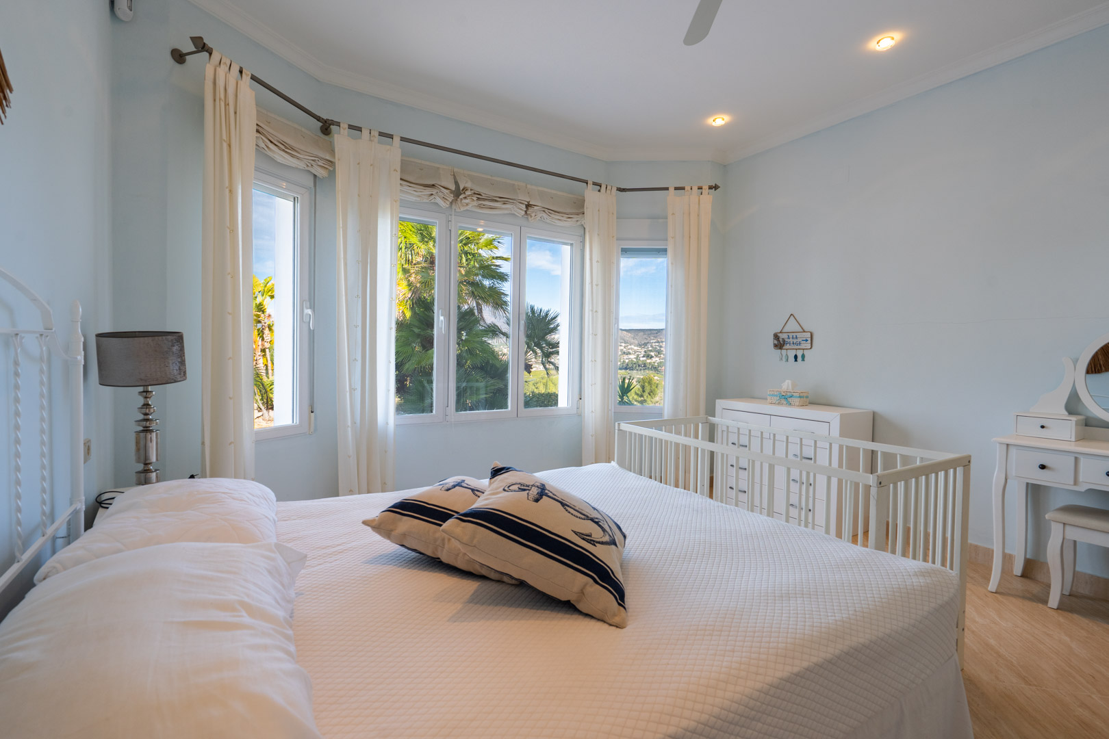 Helles Schlafzimmer mit Erkerfenster und Blick auf den Montgó, weißen Möbeln inklusive Kinderbett und Schminktisch sowie maritimen Akzenten.